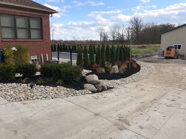New landscaping project around a residential pool in Ray Township, MI including a dry river rock bed, a boulder retaining wall, vinca vines, and emerald green arborvitaes