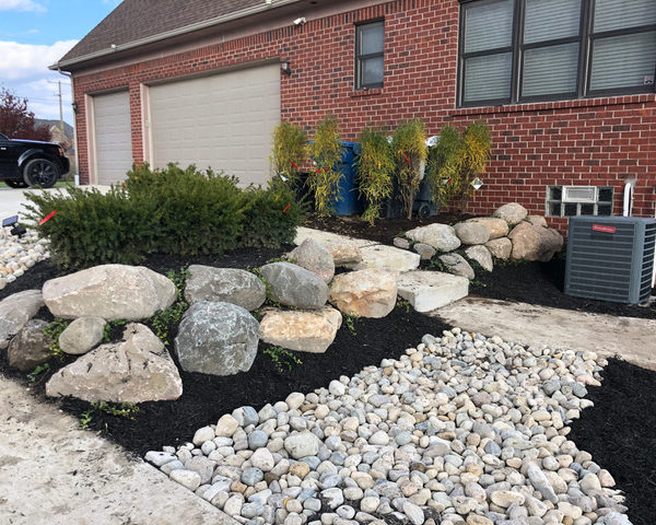 New landscaping project around a residential pool in Ray Township, MI including a dry river rock bed, a boulder retaining wall, vinca vines, and emerald green arborvitaes