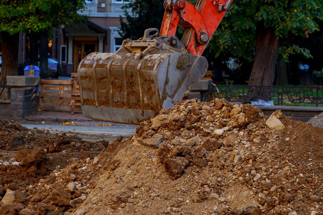 A backhoe moves dirt to prepare for a new residential landscape installation by J & J Landscaping